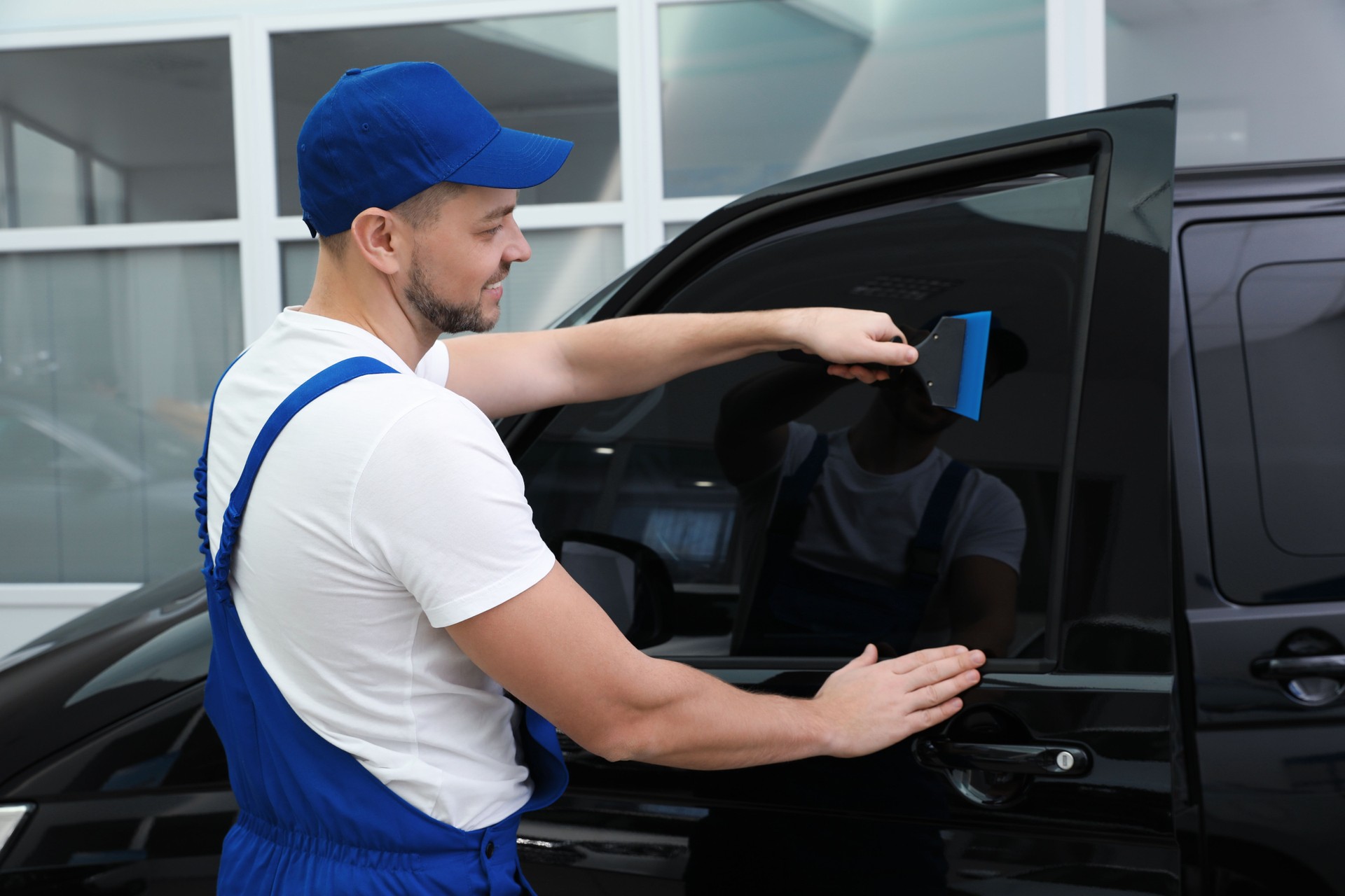 Worker tinting car window with foil in workshop